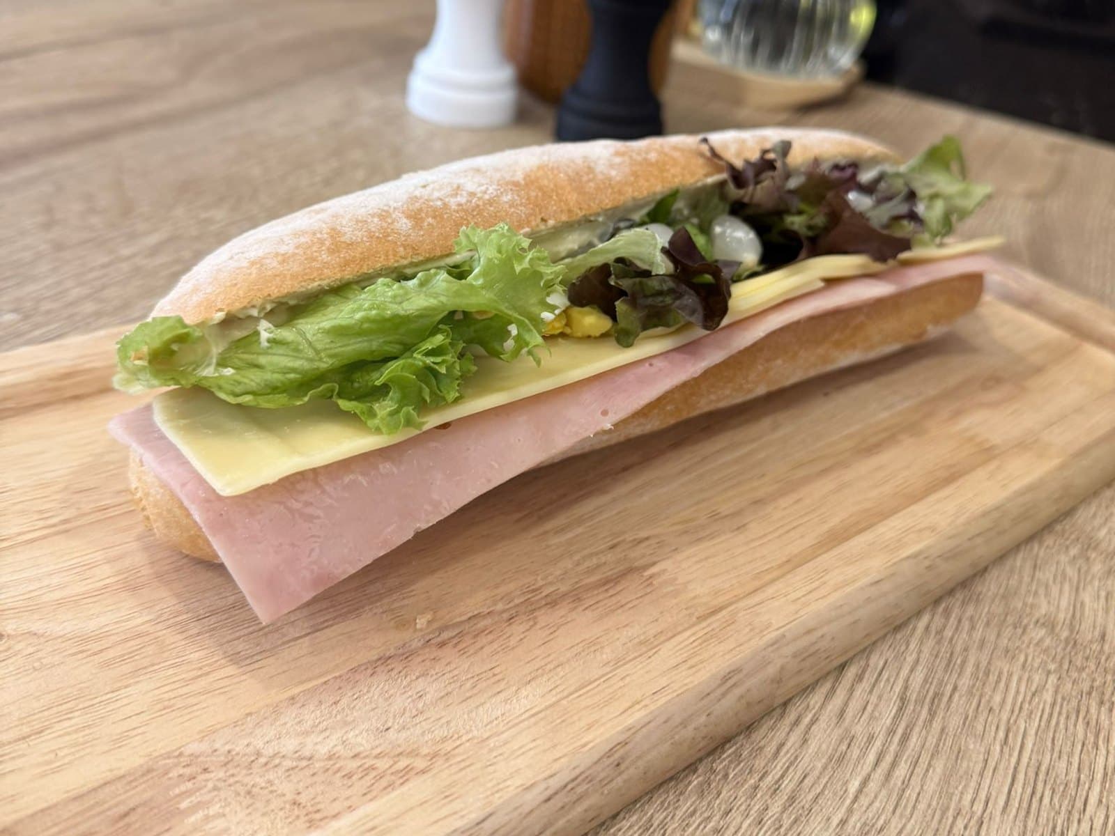 Un dagobert ouvert sur une planche en bois, jambon, fromage et salade